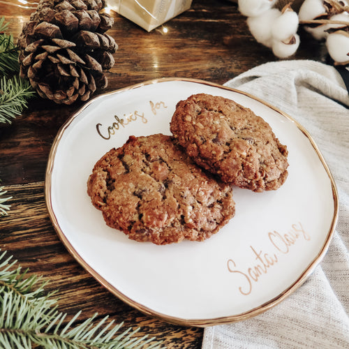 Two cookies on a white ceramic plate labeled 'Cookies for Santa Claus'. The script font as well as the edge are gold.