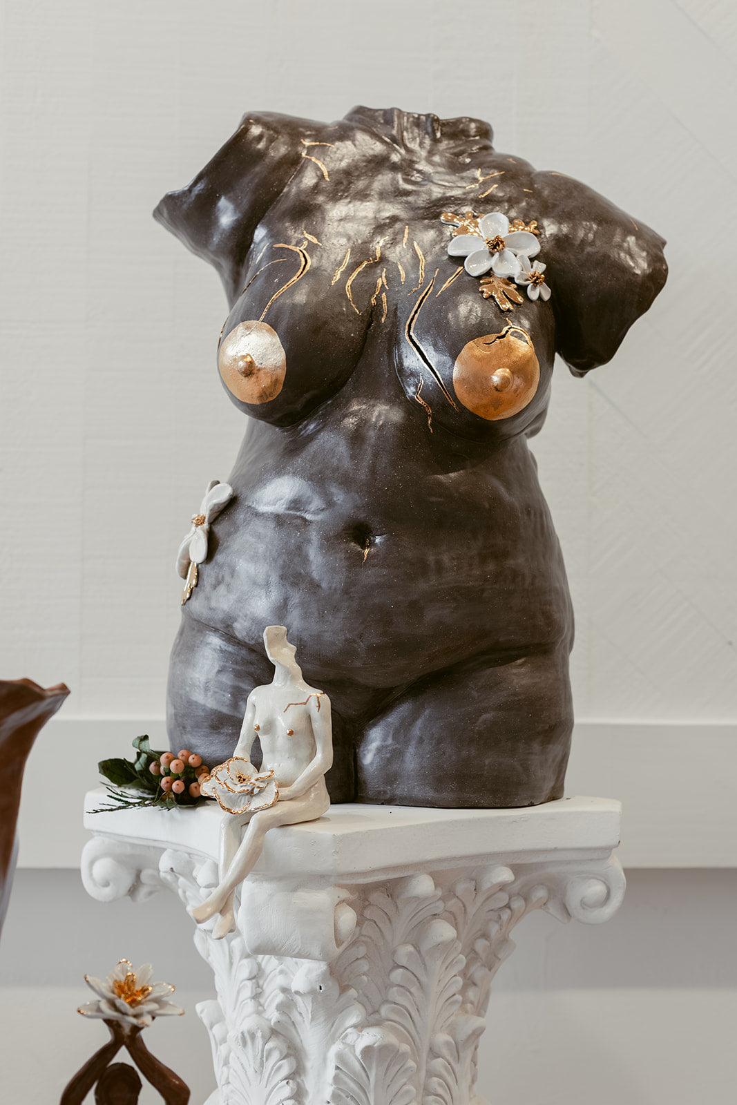 A little white sculpture positioned in front of a larger black sculpture. Both have gold accenting female features of the body.