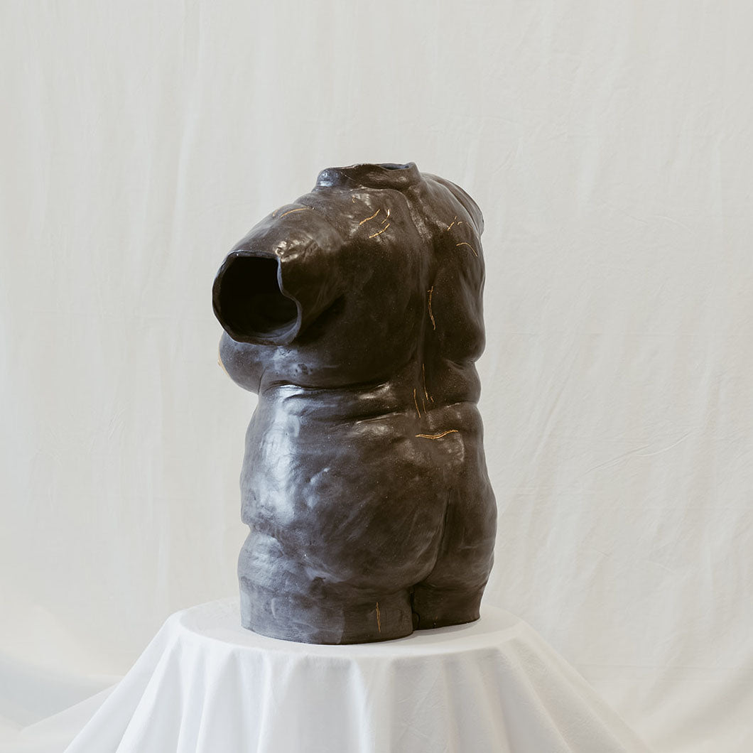 Dark sculpture of a female torso full of imperfections. We see the sculpture from the back.
