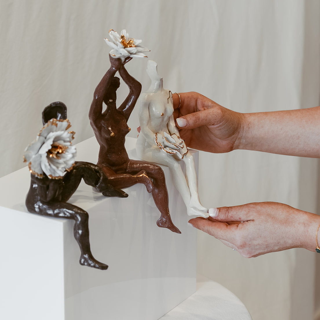 A close-up of the figurines of the piece, "She Who Gathers". There are hands placing the porcelain figurine, highlighting that each individual one is only part of the work.