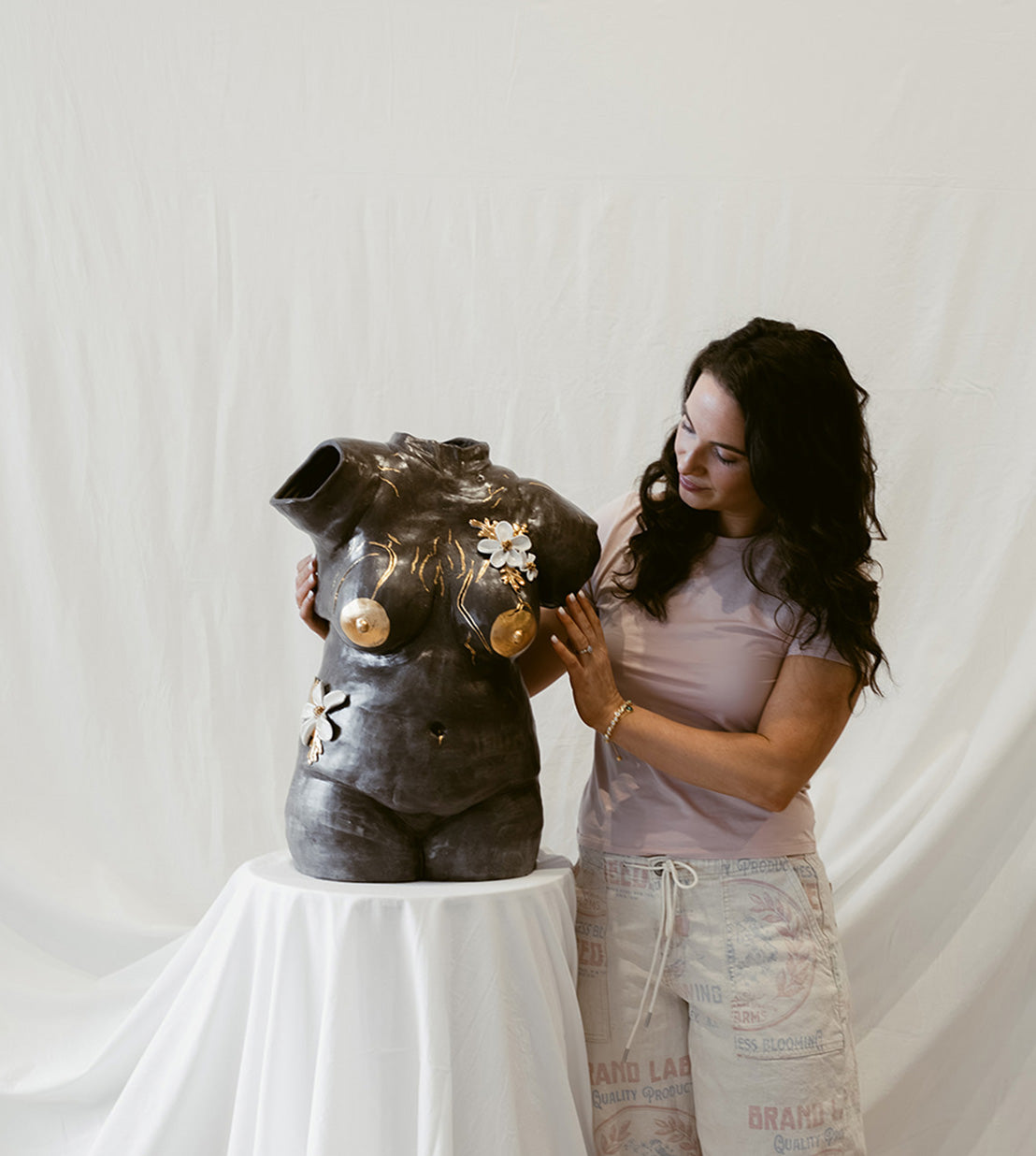 Eleni posing next to a dark ceramic bust. The sculpture has gold accents across the chest.
