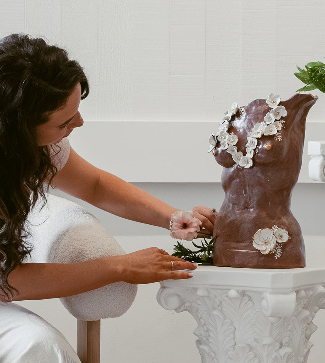 Eleni putting a real flower by one of her sculptures that has ceramic flowers with golden edges.