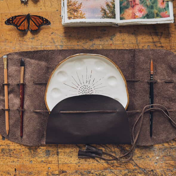 Another overhead view of the "Mary Leather Wrap". The wrap is shown with a painter's palette and paintbrushes.