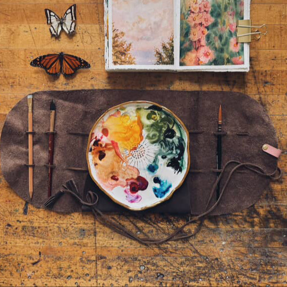 An overhead view of the "Mary Leather Wrap". The wrap is shown with a painter's palette and paintbrushes.