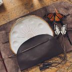 An angled overhead view of the "Mary Leather Wrap". The wrap is shown with a painter's palette and paintbrushes.