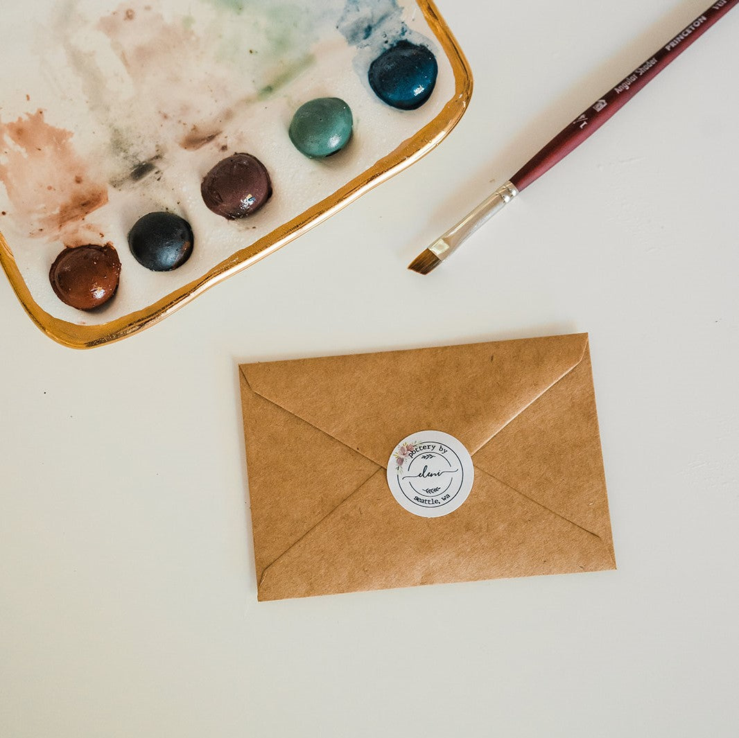 An overhead view of a brown paper envelope sealed with Eleni's sticker seal.