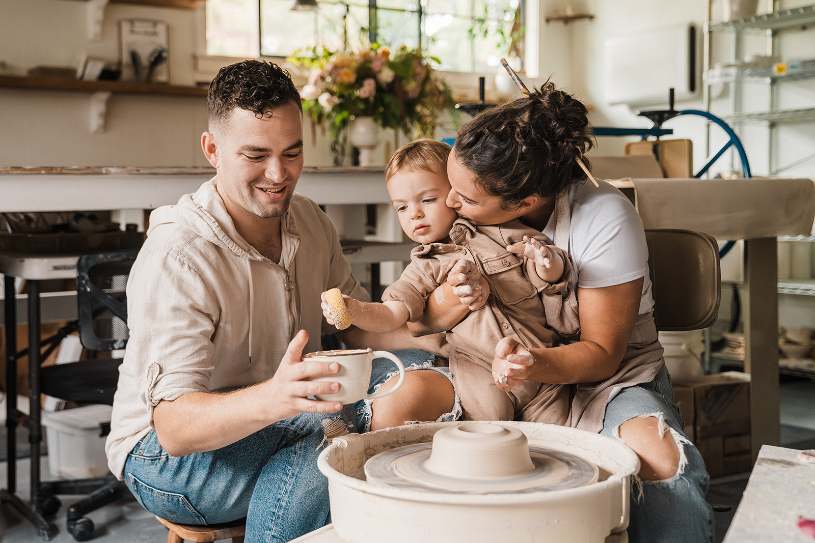 Eleni, husband, and son, smiling and interacting with a spinning pottery wheel.