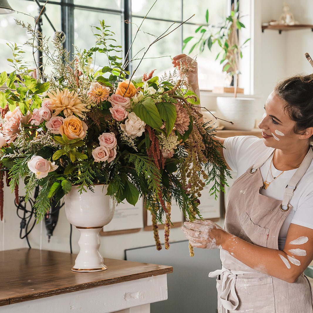 Another photo of Eleni standing beside a large floral arrangement in a white pedestal vase.