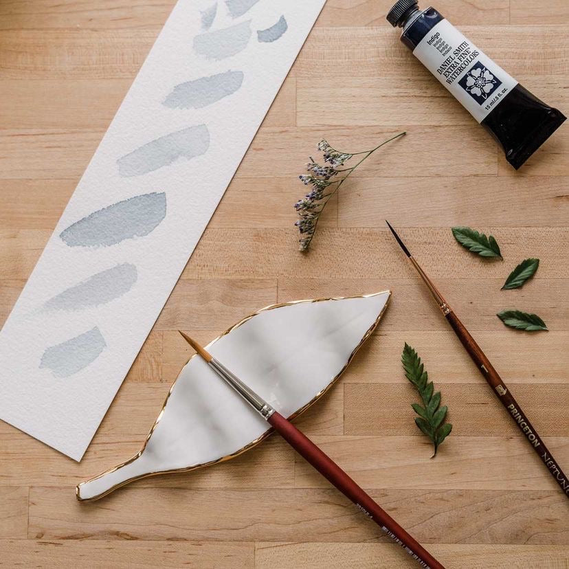 An overhead view of "The Imogene Brush Rest" an elegant, leaf-shaped rest, handcrafted from locally sourced porcelain and finished with a 22k gold edge.